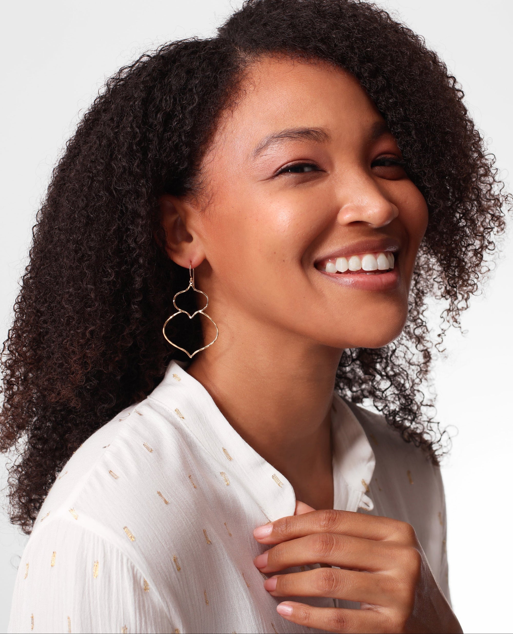 Woman with curly hair wearing a Kiara Majorelle Drop Earrings and a white blouse against a light background